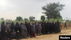 Un homme portant le drapeau de Boko Haram passe devant un groupe de 82 filles Chibok tenues en captivité pendant trois ans par des militants islamistes en attente d'être libérés en échange de plusieurs commandants militants, près de Kumshe, Nigeria, 6 mai 2017 .