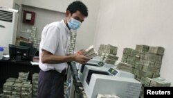 An employee counts Burmese kyat banknotes in a bank in the capital, Rangoon, April 5, 2012.