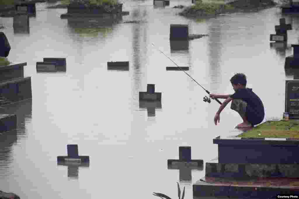 Atet Dwi Pramadia dari Indonesia meraih juara harapan lewat foto &quot;Fishing in the Cemetery&quot;, menggambarkan anak yang memancing di sebuah tempat pemakaman yang kebanjiran di Jakarta.