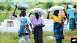 FILE - Women carry bags of maize during a food aid distribution in Mudzi about 230 kilometers northeast of the capital Harare, Zimbabwe, Feb. 20, 2020.