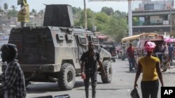 Varias personas pasan frente a un vehículo blindado de la policía que patrulla las calles de Puerto Príncipe, Haití, el lunes 15 de julio de 2024.