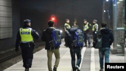 Un officier de police escorte des migrants du train de la gare de Hyllie à Malmo, en Suède, le 19 novembre 2015.