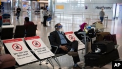 A man sits wearing a face shield in the arrivals area on the first day of new rules that people arriving in Britain from overseas will have to quarantine themselves for 14 days to help stop the spread of coronavirus, at Heathrow Airpot in London,…