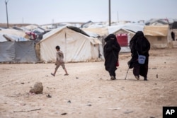 FILE - Women walk in the al-Hol camp that houses some 60,000 refugees, including families and supporters of the Islamic State group, in Hasakeh province, Syria, May 1, 2021.