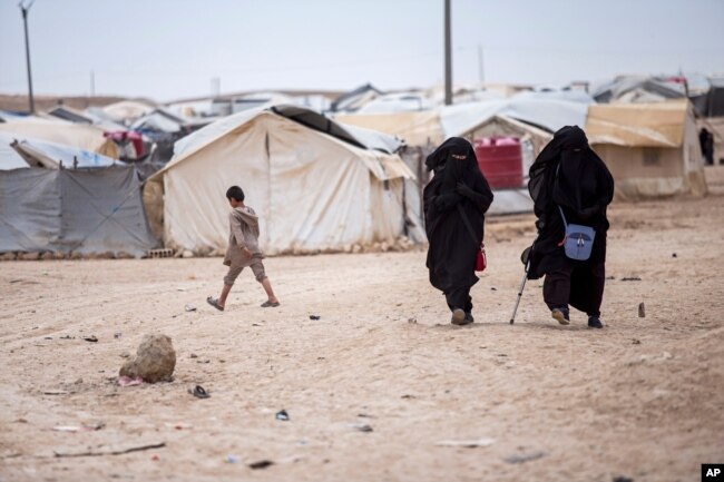 FILE - Women walk in the al-Hol camp that houses some 60,000 refugees, including families and supporters of the Islamic State group, in Hasakeh province, Syria, May 1, 2021.