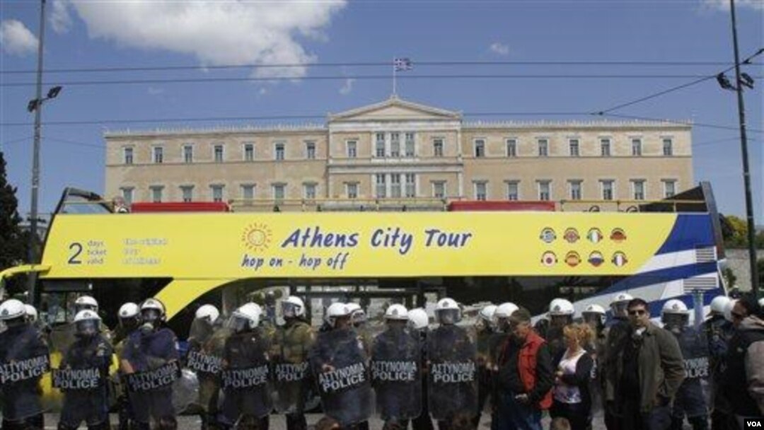 Bus touris melewati gedung parlemen Yunani sementara polisi membuat barikade bagi para demonstran di Athena.