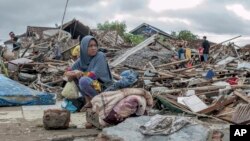 Una mujer sobreviviente del tsunami sentada sobre los escombros mientras intenta rescatar artículos del sitio donde estuvo su casa en Sumur, Indonesia, el 24 de diciembre de 2018.