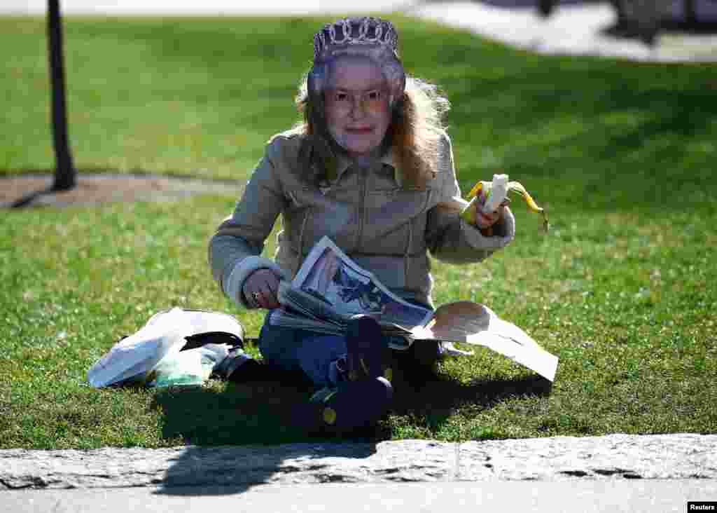A woman wearing a mask of Britain&#39;s Queen Elizabeth reads a newspaper near Tower bridge in London.