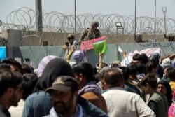 Un soldado estadounidense sostiene un letrero que indica que una puerta está cerrada mientras cientos de personas reúnen algunos documentos, cerca de un puesto de control de evacuación en el perímetro del aeropuerto de Kabul el 26 de agosto de 2021.