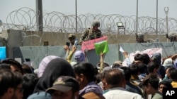 Un soldado estadouniense sostiene un letrero que indica que una puerta está cerrada mientras cientos de personas reúnen algunos documentos, cercaa de un puesto de control de evacuación en el aeropuerto de Kabul el 26 de agosto de 2021.