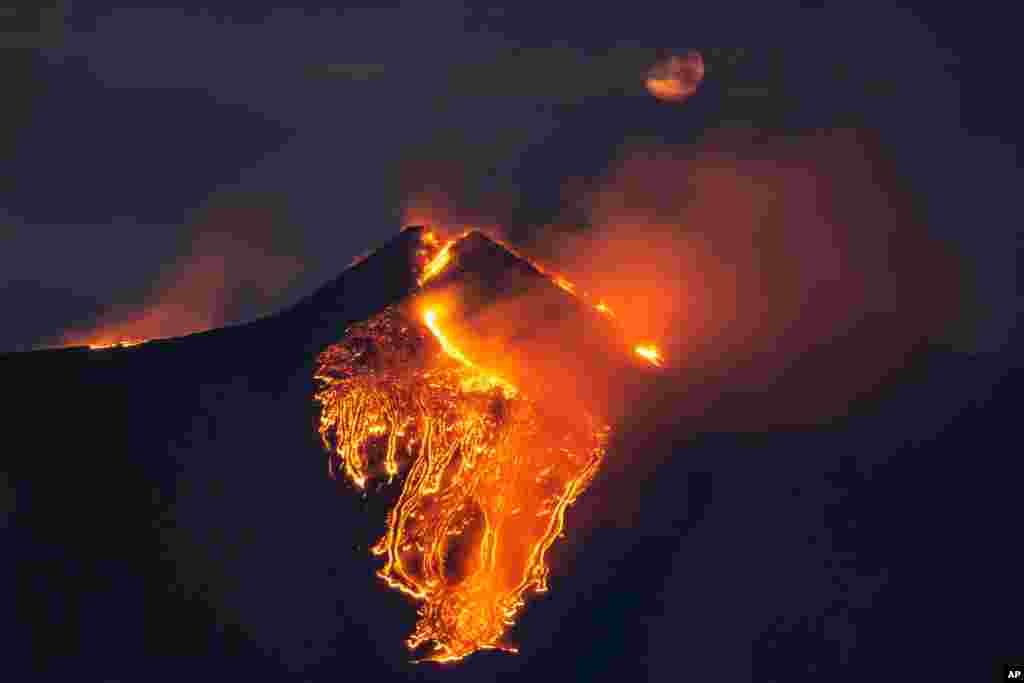 The moon is partially seen in the sky as lava flows from the Mount Etna volcano, near Catania, Sicily, Italy.