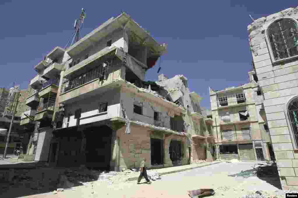 A man walks pasts damaged buildings in the old city of Aleppo, July 3, 2013.
