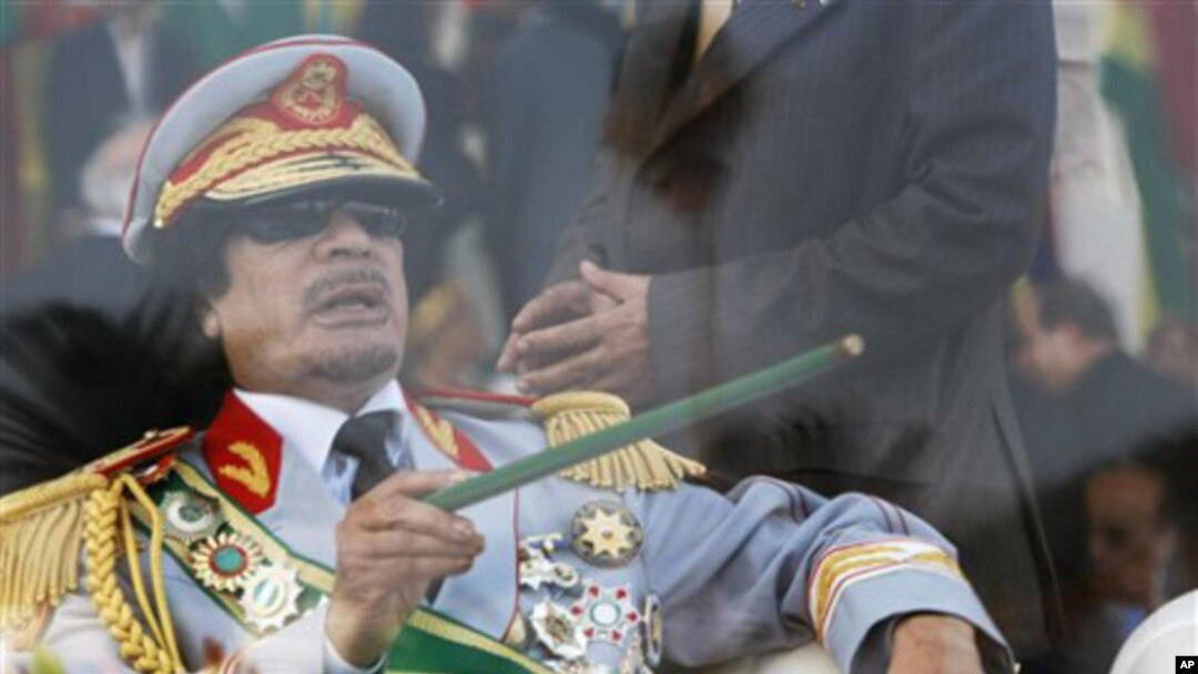 In this Sept. 1, 2009 file photo, Libyan leader Moammar Gadhafi gestures with a green cane as he takes his seat behind bulletproof glass for a military parade in Green Square, Tripoli, Libya.