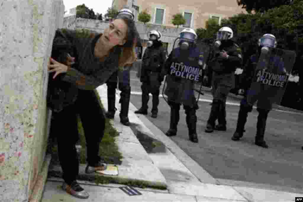 A protester takes cover in front of riot police during clashes in Athens, Wednesday, Feb. 23, 2011. Scores of youths hurled rocks and petrol bombs at riot police after clashes broke out Wednesday during a mass rally taking place as part of a general strik