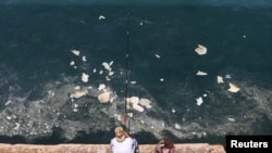 FILE - A fisherman dangles his line to catch fish in polluted water off Beirut's seaside Corniche, Lebanon, June 23, 2019. 