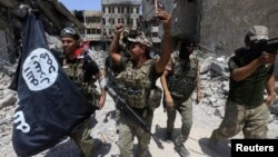 FILE - Members of Iraq's Emergency Response Division hold an Islamic State flag that they pulled down as they celebrate in the Old City of Mosul, Iraq, July 8, 2017. Islamic State fighters have mostly been pushed out of Iraq and Syria but are far from defeated.