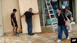 James Fujita, left, and Reid Fujita take down plywood boards that were to protect their store from Tropical Storm Lane along Waikiki Beach, Aug. 25, 2018, in Honolulu. 