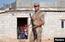 FILE - Locals look on as a Turkish soldier stands guard in a border village on the Turkish-Syrian border near Akcakale in Sanliurfa province, Turkey, Sept. 8, 2019.