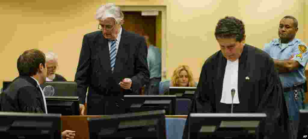 Radovan Karadzic, standing at left, talks to Marko Sladojevic, left, a member of his legal team while his legal advisor Peter Robinson, right, prepares ahead of the start of Karadzic&#39;s defense.