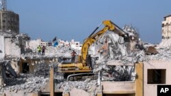 FILE- Palestinian workers use a backhoe to break and remove parts of the Al-Jawhara building, that was damaged in Israeli airstrikes during Israel's war with Gaza's Hamas rulers last May, in the central al-Rimal neighborhood of Gaza City, Nov. 16, 2021. 