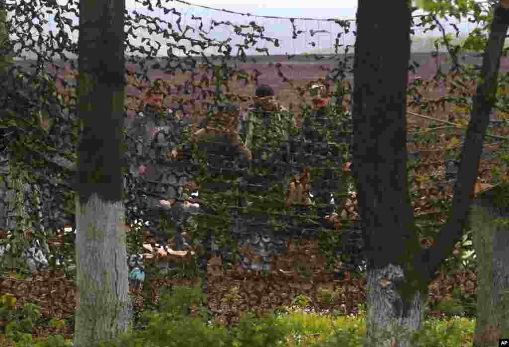 Seen through a car window, Ukrainian government troops stand behind a camouflage net as they guard a checkpoint near the village of Dolina, 30 kilometers from Slovyansk, Ukraine, April 29, 2014.