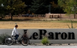 A woman cycles past a sign of the Colonia LeBaron, a community settled by members of the extended LeBaron family in Chihuahua state in northern Mexico, Nov. 6, 2019.