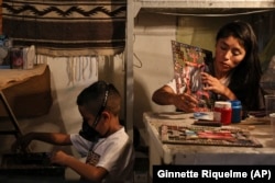 Dana Lopez, right, paints a board for poleana while her son Kevin plays in their workshop in the State of Mexico, Mexico, Friday, Oct. 25, 2024. (AP Photo/Ginnette Riquelme)