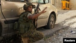 A Lebanese army soldier takes a position behind a car near the mosque complex (background), where hardline Sunni cleric Sheikh Ahmed al-Assir was believed to be sheltering with his supporters in Abra near Sidon, southern Lebanon, June 24, 2013.