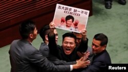 Un legislador prodemocracia es escoltado por agentes de seguridad en la Legislatura el 17 de octubre portando un cartel de la jefa ejecutiva Carrie Lam con las manos manchadas de sangre.