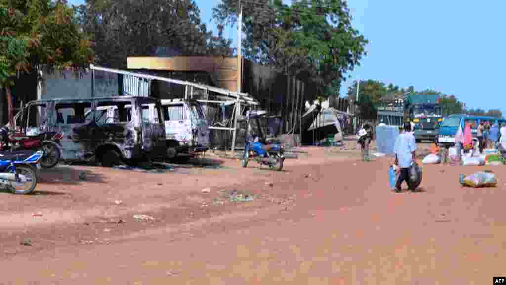 People walk past vehicles and shops burnt by Boko Haram Islamists on a street of Benisheik.