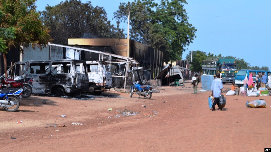 Warga berjalan melintasi kendaraan-kendaraan dan toko-toko yang dibakar oleh kelompok militan Islam Boko Haram di kota Benisheik, 19/9/2013.