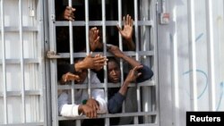 FILE - Illegal migrants, who have been detained after trying to get to Europe, look out of barred door of a detention hut at a detention camp in Gheryan, outside Tripoli, Libya.