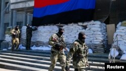 Pro-Russian armed men walk past activists hanging up a "Donetsk Republic" flag outside the mayor's office in Slovyansk, eastern Ukraine, April 21, 2014. 