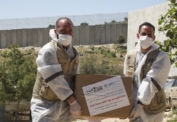 Members of the French Action Against Hunger NGO distribute hygiene and sanitation products to Palestinian residents of al-Ramadin village amid the coronavirus (COVID-19) pandemic, southwest of the West Bank town of Hebron, April 13, 2020.