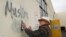 FILE - Tom Garing cleans up racist graffiti painted on the side of a an Islamic center in what officials are calling an apparent hate crime, Feb. 1, 2017, in Roseville, California. The Tarbiya Institute was spray-painted with a dozen obscene and racist slurs. Garing, a retiree who lives in the area and is not a member of the mosque, volunteered to help clean up.