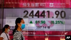 People wearing face masks walk past a bank electronic board showing the Hong Kong share index at Hong Kong Stock Exchange Monday, April 20, 2020.