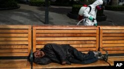 Seorang petugas kebersihan kota menyemprotkan disinfektan sementara seorang pria tidur di bangku di Plaza de Armas, di Santiago, Chili, 15 April 2020.