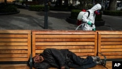 A city worker sprays disinfectant while a man sleeps on a bench in the Plaza de Armas in Santiago, Chile, April 15, 2020.