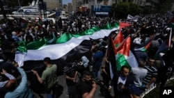 Warga Palestina berbaris membawa bendera nasional mereka dalam unjuk rasa memperingati 75 tahun apa yang mereka sebut "Nakba," atau "malapetaka", di Kota Ramallah, Tepi Barat, Senin, 15 Mei 2023. (Foto: AP)