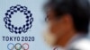 Un homme portant un masque facial marche devant un panneau d'affichage avec le logo des Jeux olympiques de Tokyo 2020, à Tokyo, au Japon, le 2 avril 2020. (AP)