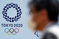 FILE - A man wearing a face mask walks passed a billboard with the logo of the Tokyo 2020 Olympics, in Tokyo, Japan, April 2, 2020.