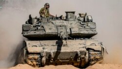 Israeli soldiers drive a tank at a staging ground near the border with the Gaza Strip, in southern Israel, May 5, 2024.