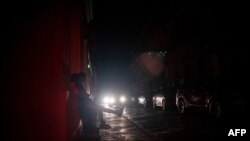 People sit on the sidewalk of a street left in darkness by a power outage in Old San Juan, Puerto Rico, June 10, 2021. 