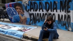 Seorang fan dari bintang sepak bola Diego Maradona duduk di dekat bendera yang dipasang di luar gedung pengadilan di pinggiran Buenos Aires, Argentina, pada 11 Maret 2025. (Foto: AP/Natacha Pisarenko)