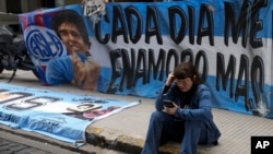 Seorang fan dari bintang sepak bola Diego Maradona duduk di dekat bendera yang dipasang di luar gedung pengadilan di pinggiran Buenos Aires, Argentina, pada 11 Maret 2025. (Foto: AP/Natacha Pisarenko)