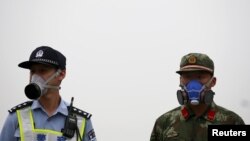 Seorang hansip dan polisi China, keduanya mengenakan masker berjaga di dekat lokasi ledakan di distrik Binhai, Tianjin, China hari Selasa (18/8). 