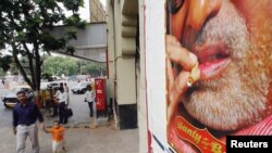 Seorang pria dan anak berjalan di depan poster iklan menunjukkan bintang Bollywood Bachchan merokok di salah satu filmnya, di Bombay, India.