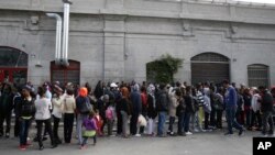 FILE - Migrants queue waiting to enter the refectory at a refugee hub in Milan, Italy, Oct. 21, 2016. A 25-year-old woman from the Ivory Coast reportedly died on Monday afternoon at a migrant center in Cona, near Venice, triggering a protest over living conditions.