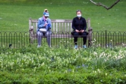 Two people sit on a bench as they wear protective masks and practice social distancing amid the coronavirus pandemic, at St. James's Park, in London, Britain, April 16, 2020.
