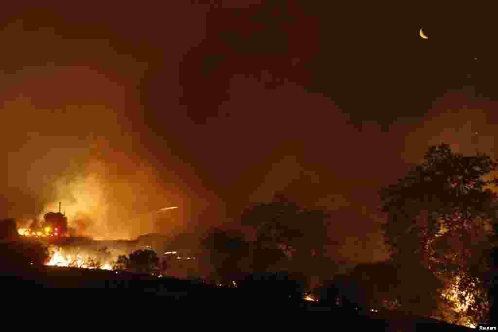 A crescent moon rises above a backfire started into the Santa Monica Mountains off Potrero Road near Newbury Park, California as a fire ignition flare is fired from the road.